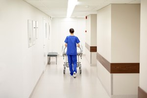 En sykepleier triller en seng ned en korridor. Foto: Mostphotos.