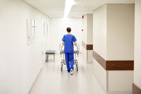 En sykepleier triller en seng ned en korridor. Foto: Mostphotos.