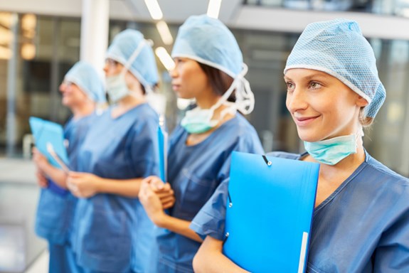 Fire kirurger/kirurgiske sykepleiere står ved siden av hverandre og holder på en mappe. Foto: Mostphotos.