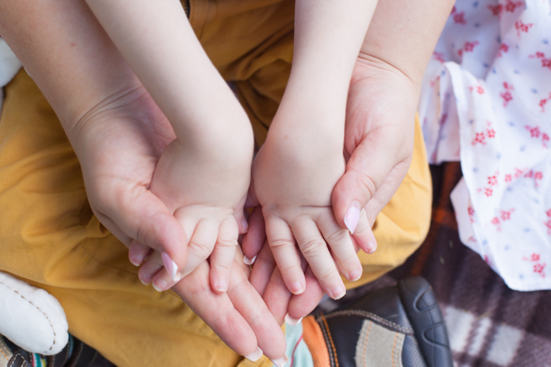 En voksen kvinne holder hendene til et barn. Foto: Mostphotos.