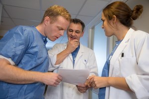 Tre helsepersonell står og ser på et papir og snakker sammen sammen. Foto: Mostphotos.