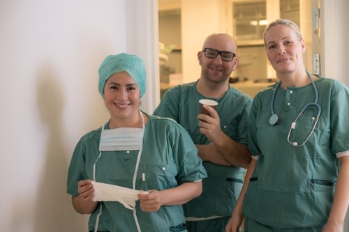 Tre helsepersonell står sammen utenfor en operasjonssal. Alle ser på fotografen. Foto: Mostphotos.